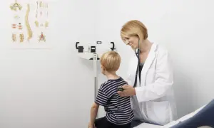 Lekarka bada chłopca stetoskopem. Obok stoi waga lekarska, co to jest bilans u lekarza.